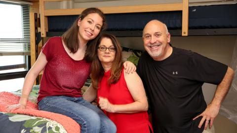 Student with parents sit on bed in dorm on move in day
